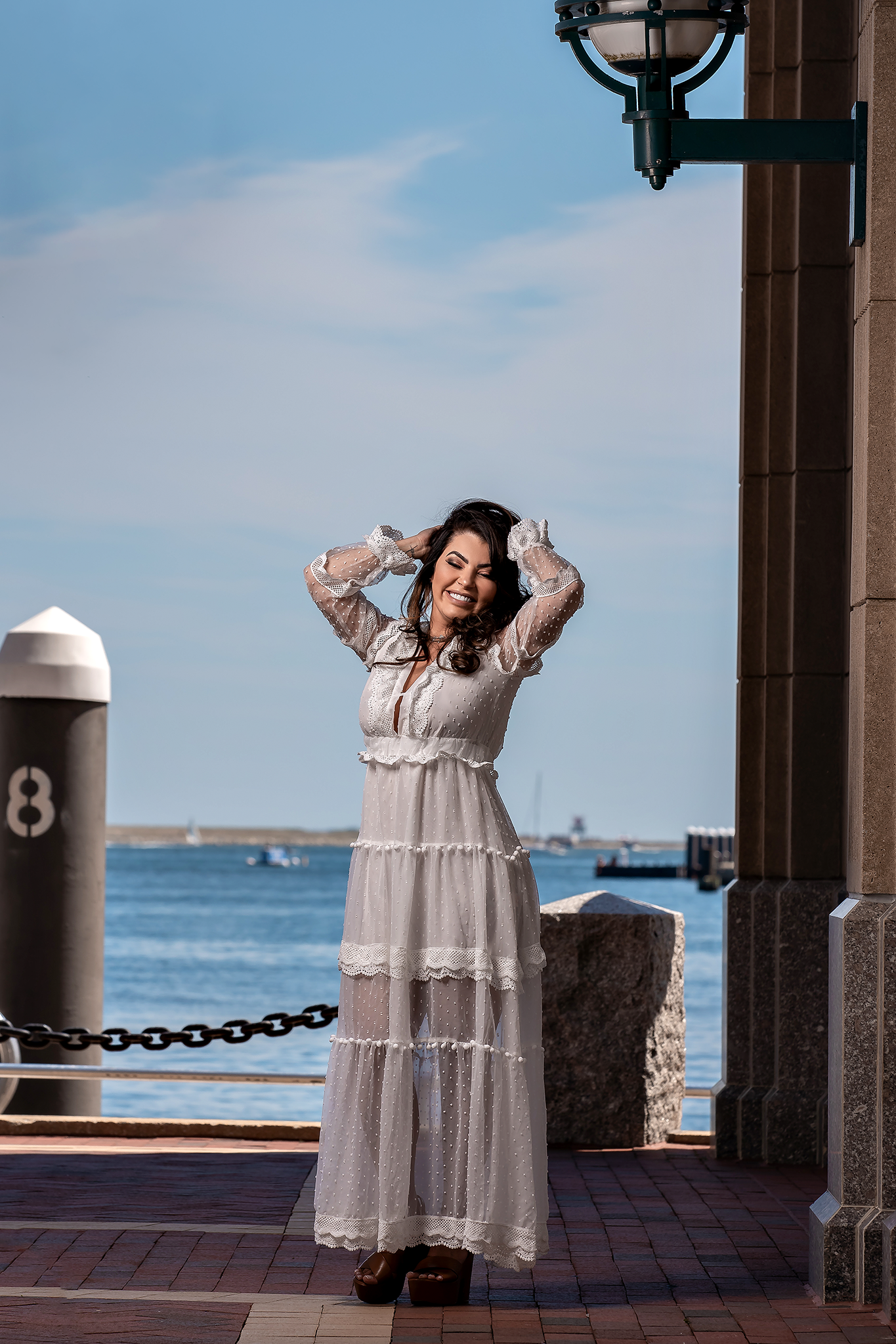 Person in flowing white dress poses on wooden pier by ocean.
