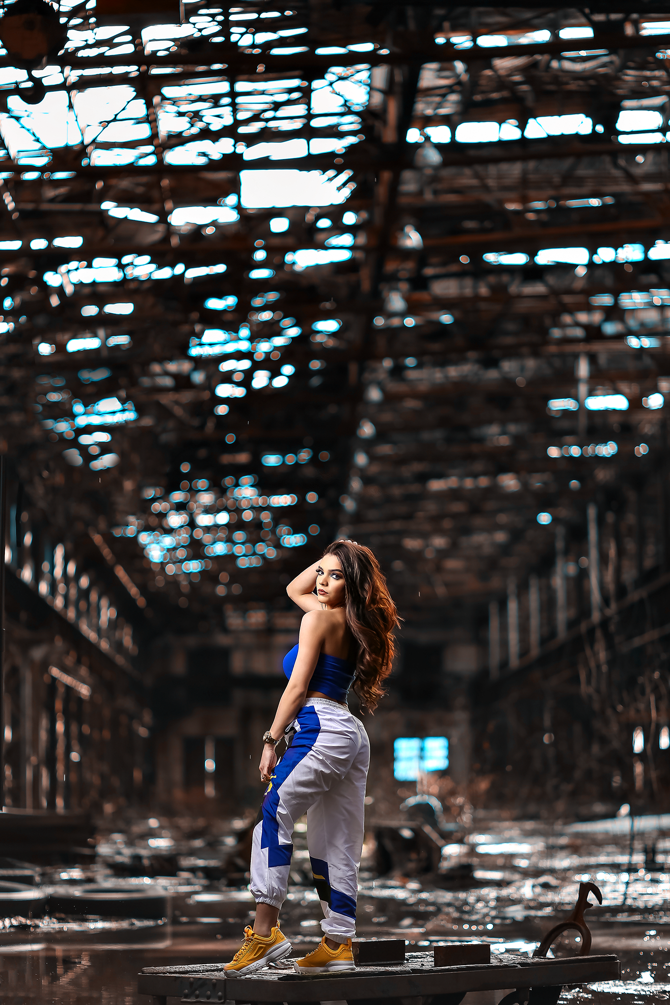 Woman in athletic wear poses inside an abandoned industrial building with dramatic lighting.