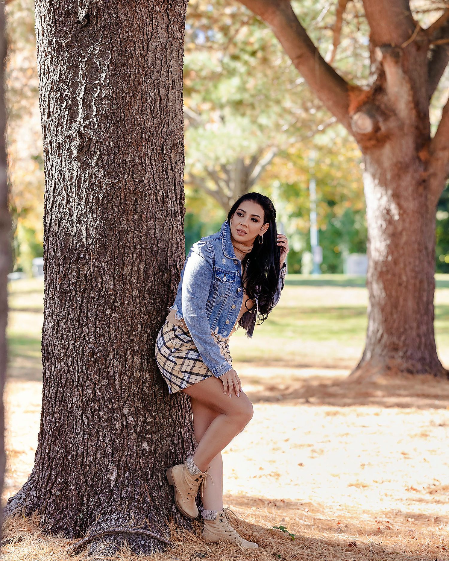 Fashion photoshoot in a park featuring artistic poses against large tree trunks in autumn sunlight.