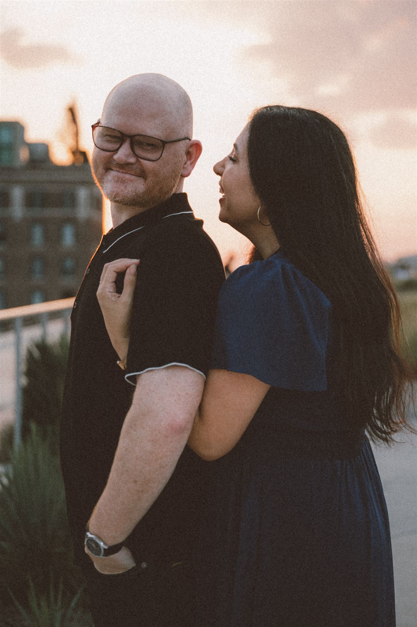 Romantic couple embrace during sunset on an urban rooftop garden.