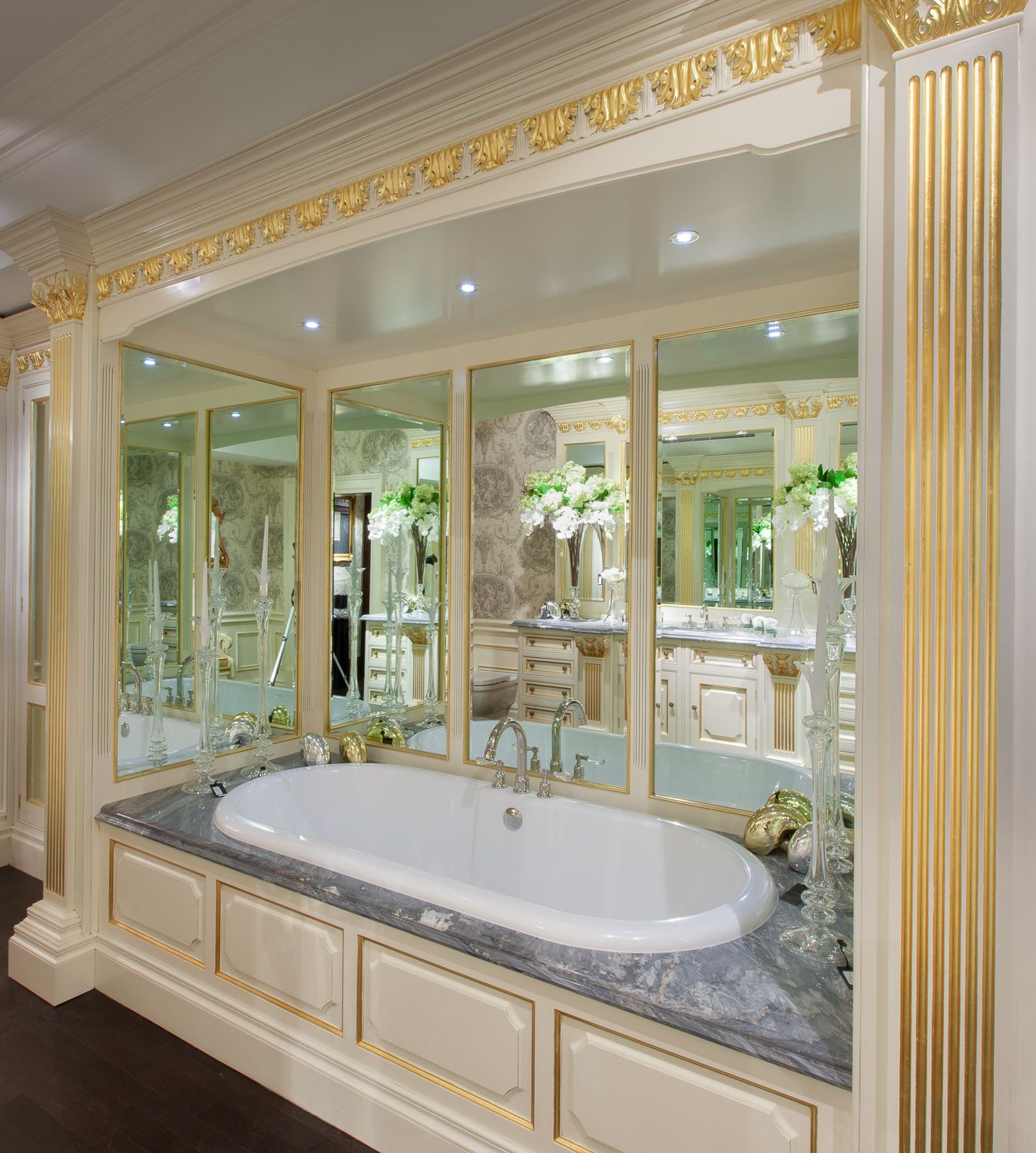 Luxurious marble bathroom with ornate gold trim and mirrored walls features an elegant built-in soaking tub.