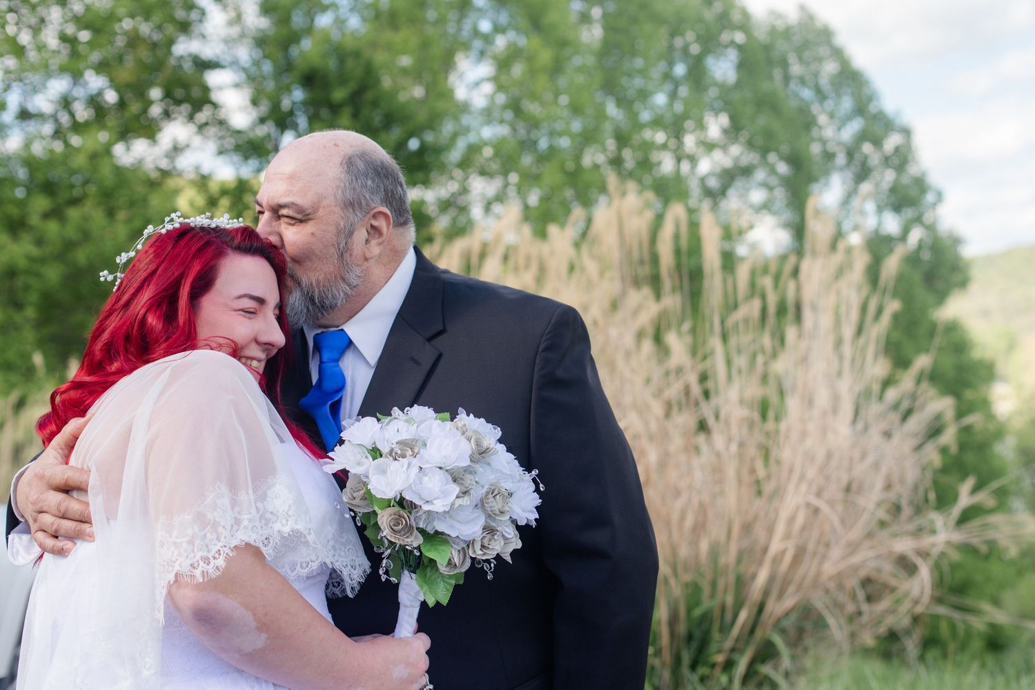 Wedding couple embracing outdoors against a natural backdrop with white floral arrangements.