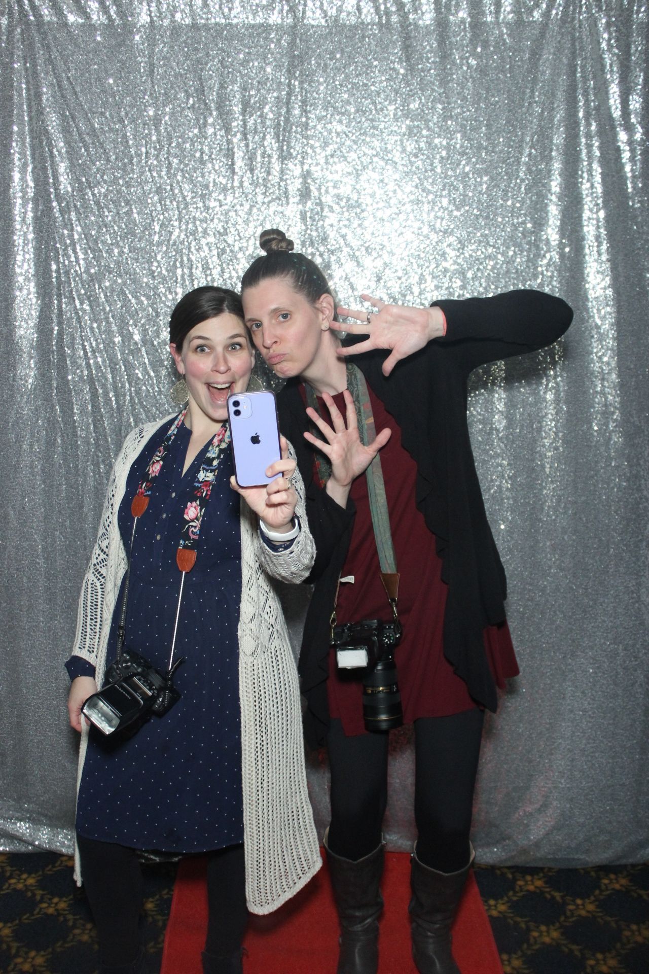 Two photographers posing with cameras against a silver sequin backdrop.