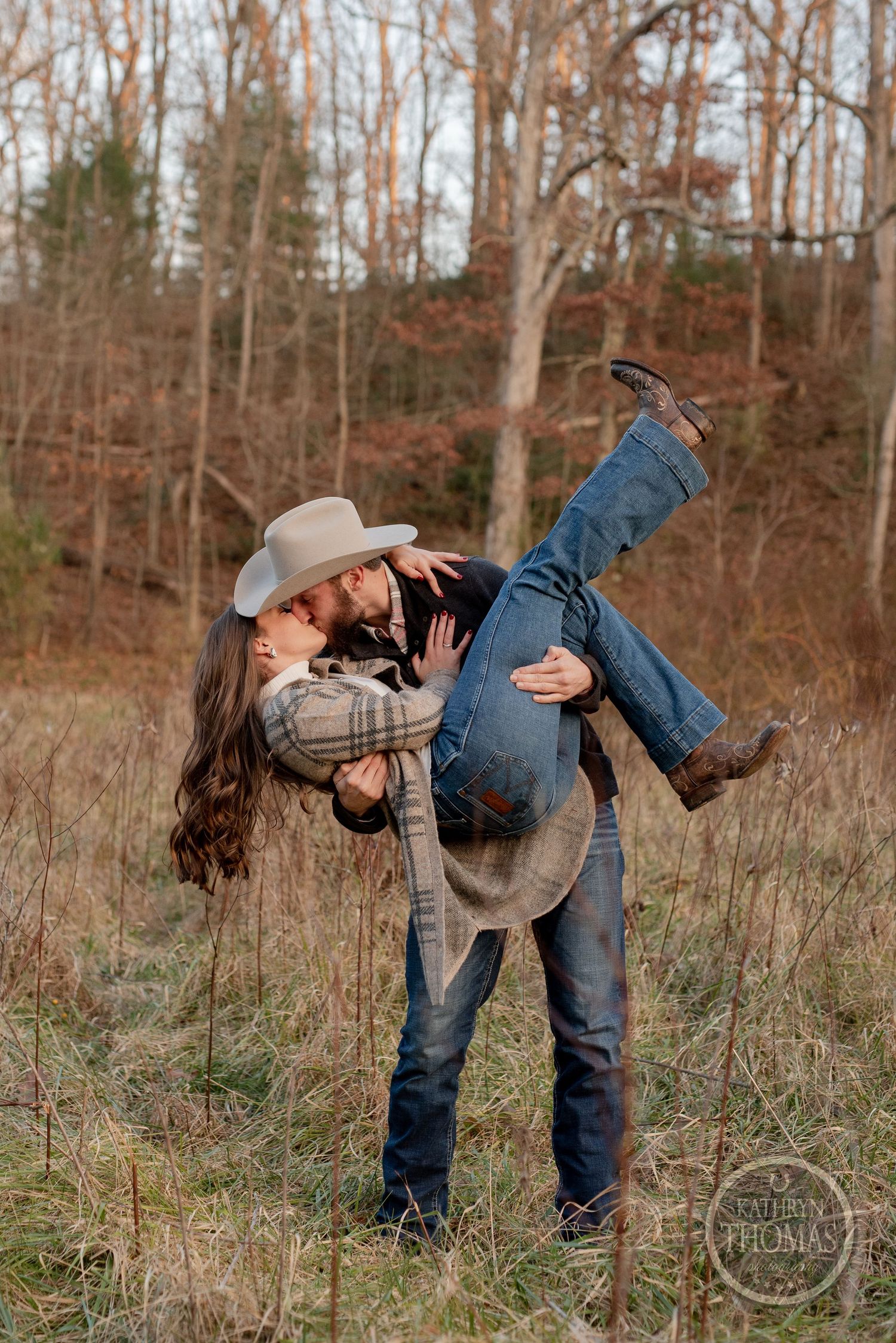 A playful dip pose with a cowboy hat in a rustic outdoor setting.