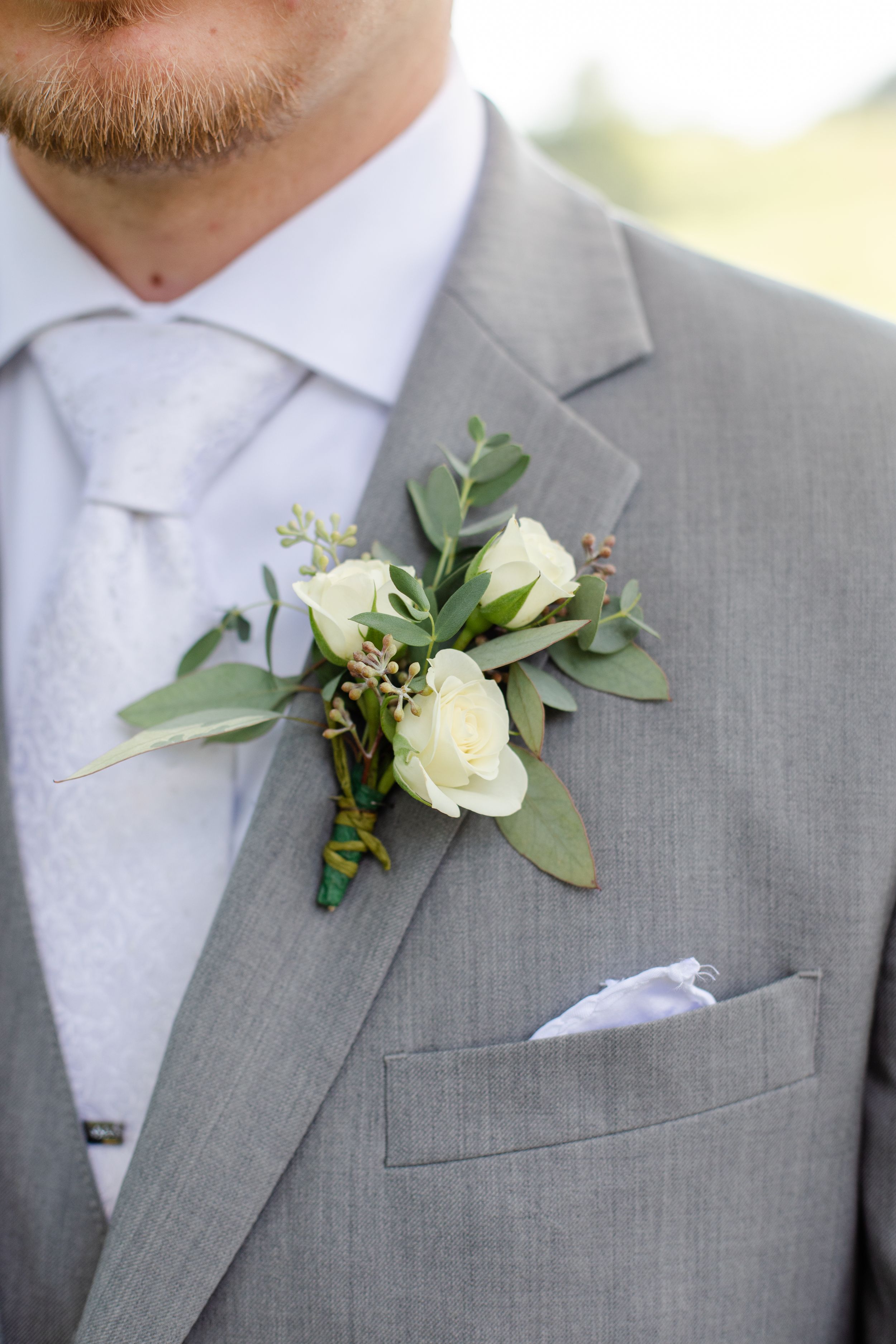 Elegant white floral boutonnieres with eucalyptus leaves pinned to light grey suit lapels.