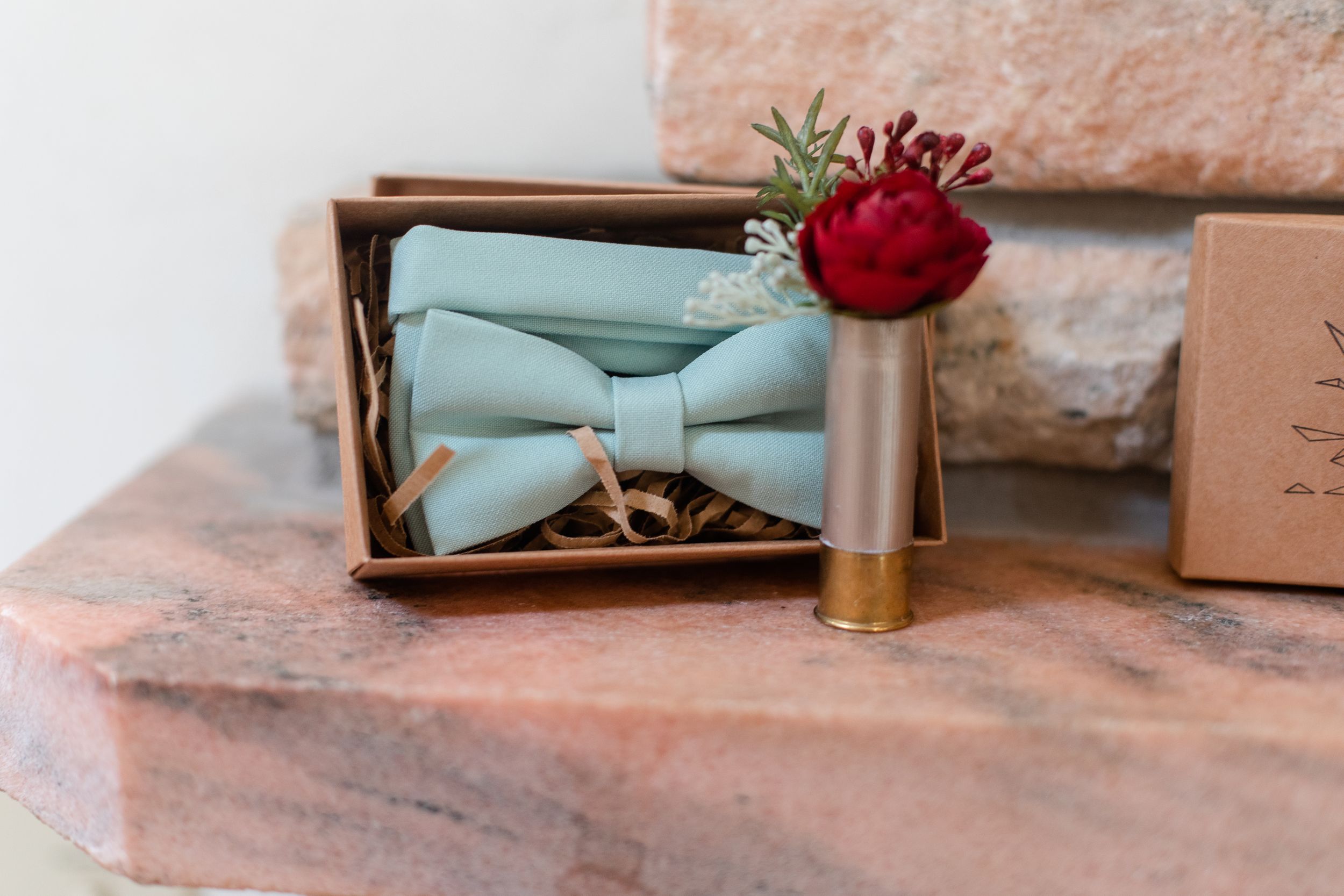 Mint green bow ties and wedding accessories arranged on peach-colored surface.