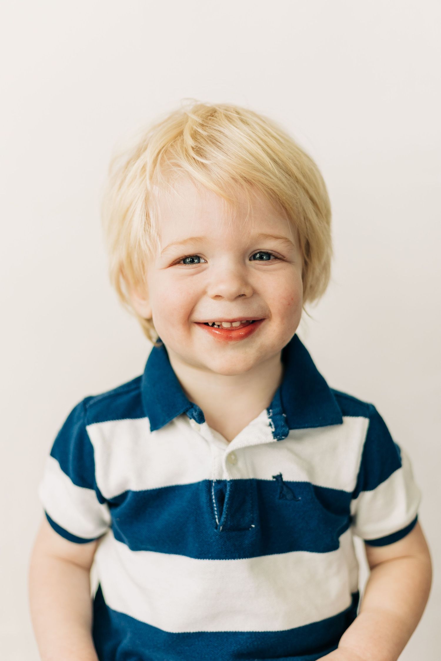 A young child wearing a navy and white striped polo shirt smiles brightly against a light background.