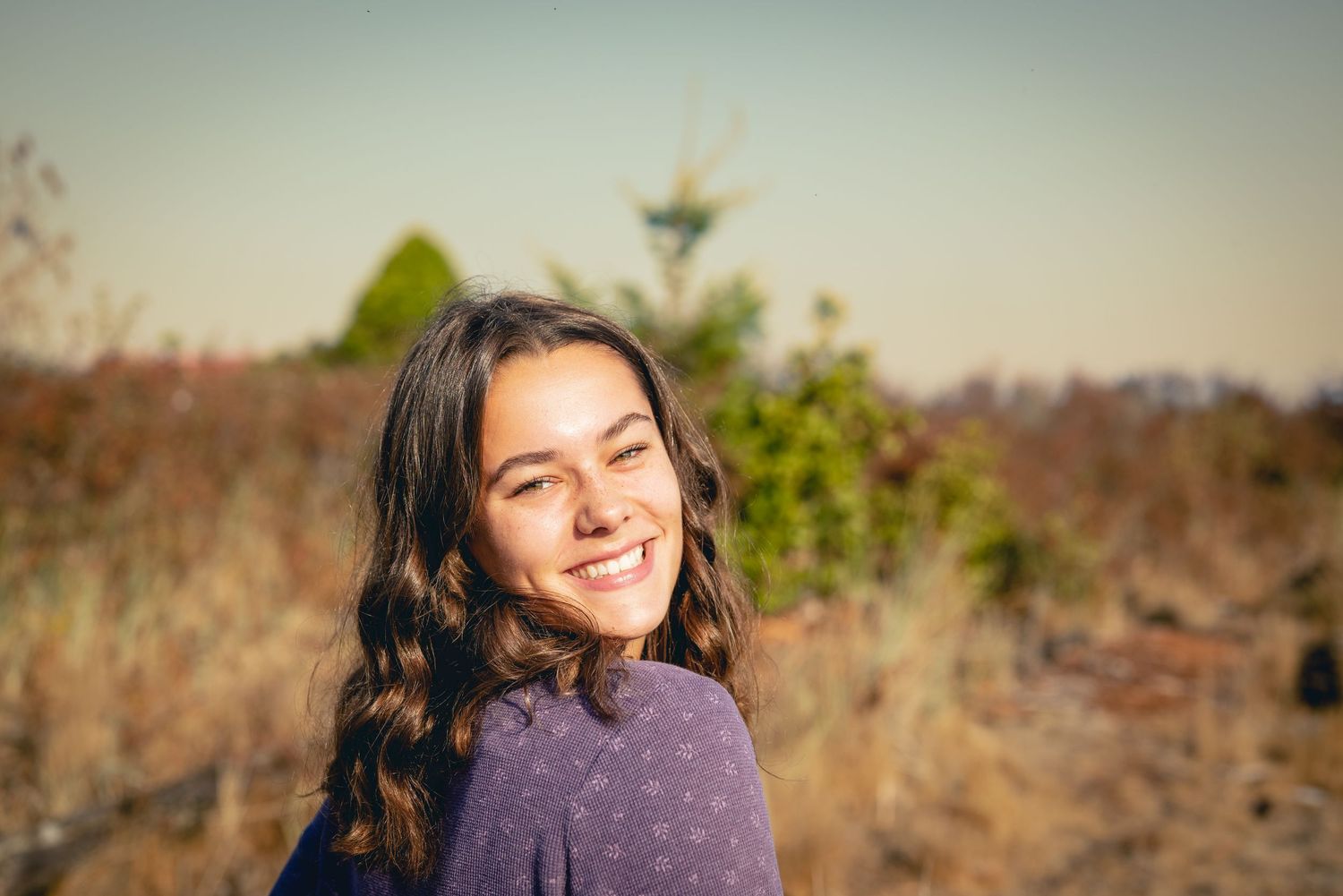 Outdoor portrait in natural lighting with soft warm tones and desert brush background.