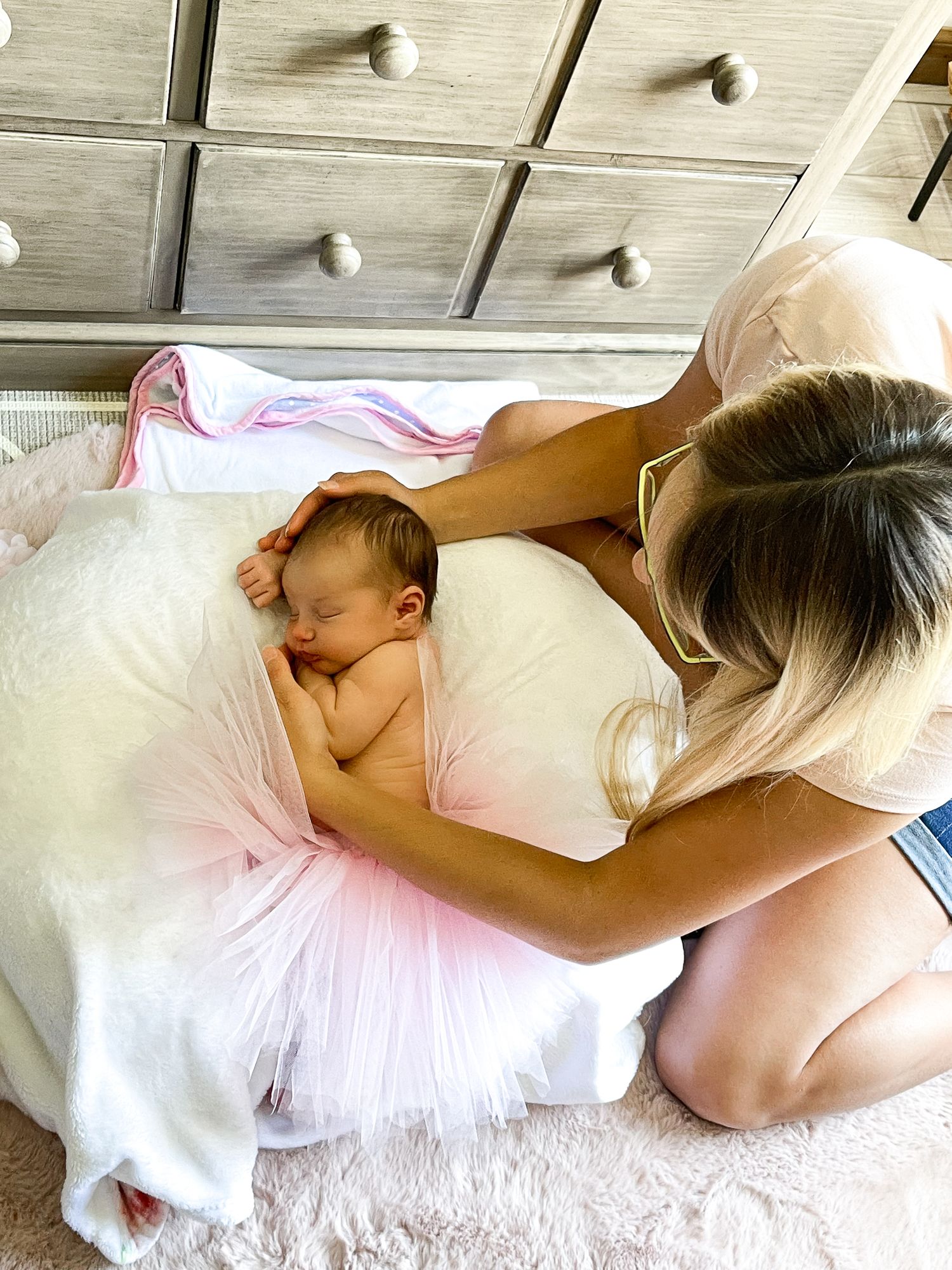 Tender moment during newborn photoshoot on white blanket with pink tulle accents.