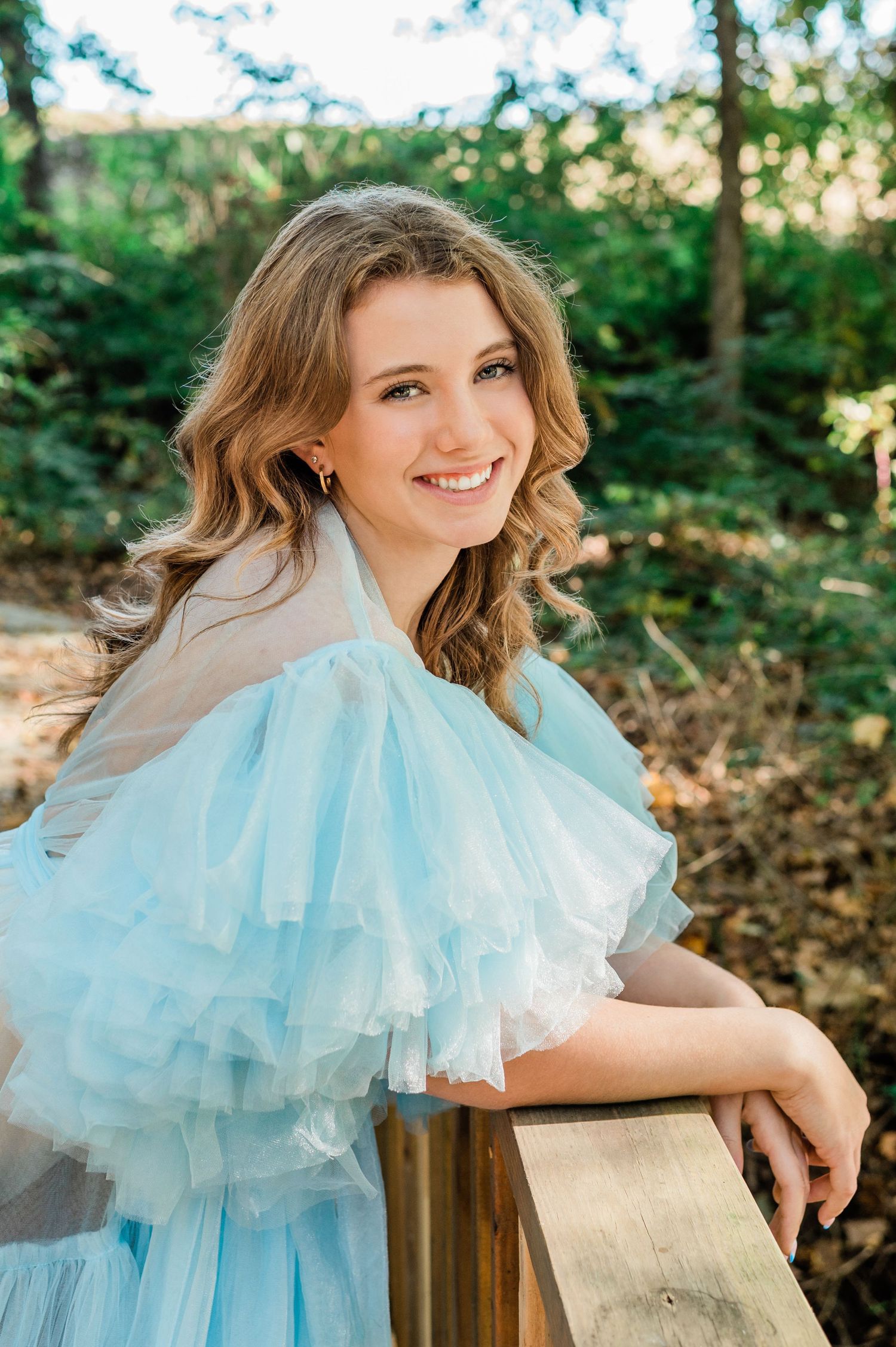 Romantic portrait series featuring light blue tulle gown against wooden railing in garden setting.