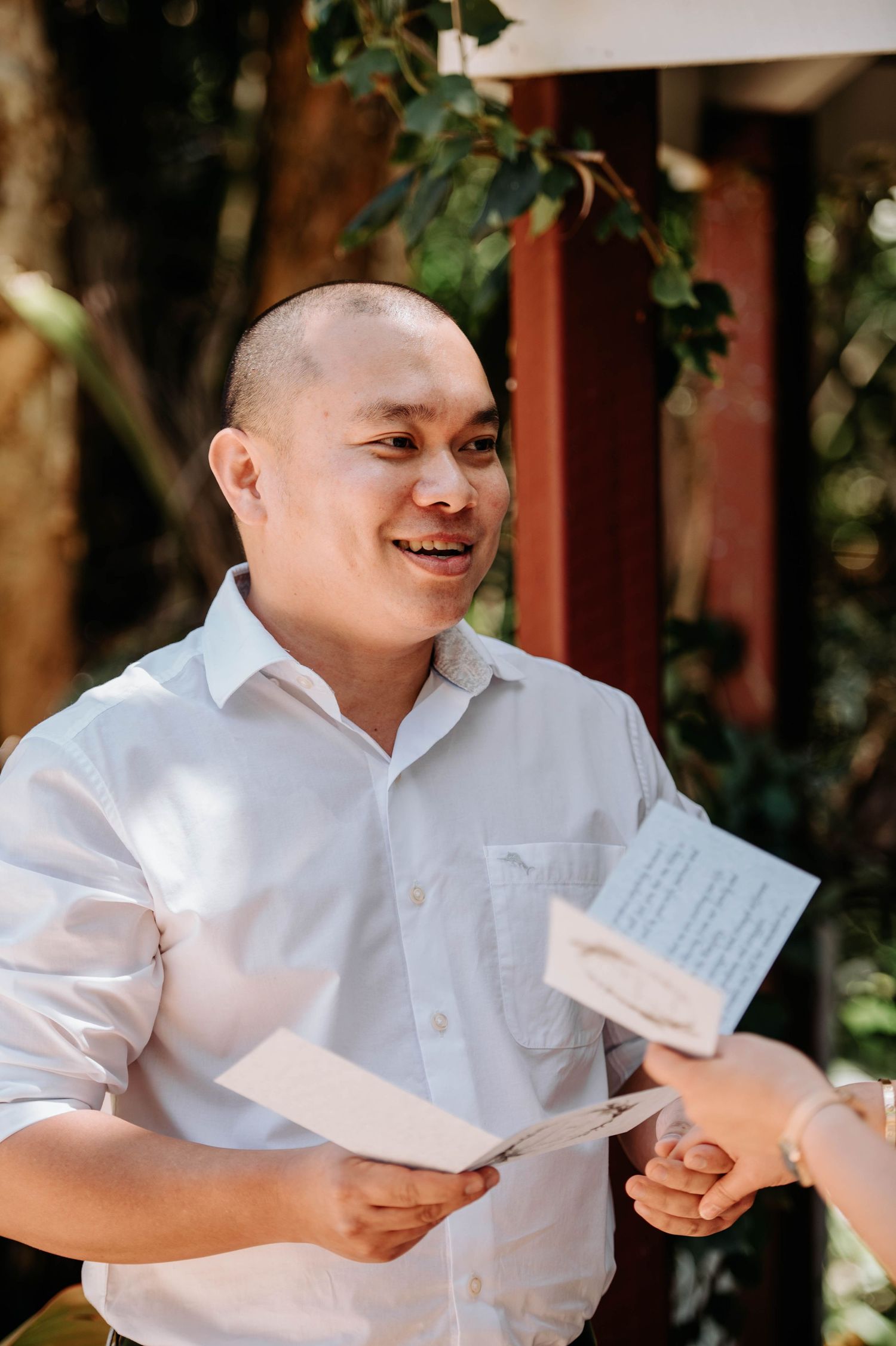 Person in white shirt reads from paper during outdoor ceremony with natural lighting.