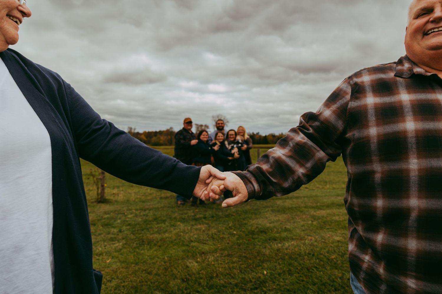 Close-up of hands clasped together with people in background on grassy field.