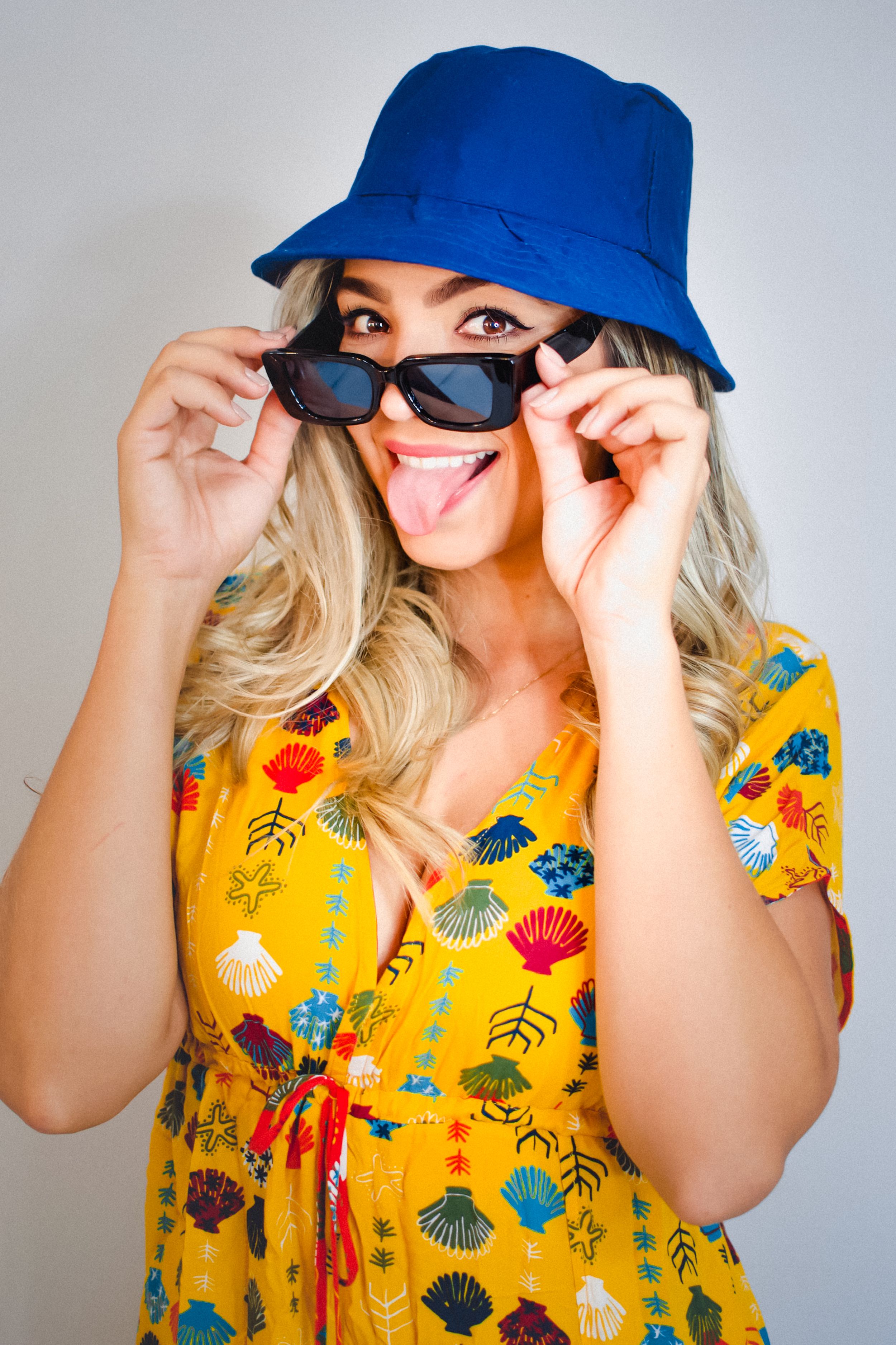 Playful summer look with blue bucket hat, sunglasses and yellow floral dress.
