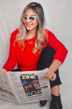 Casual portrait in red sweater holding newspaper against light background.