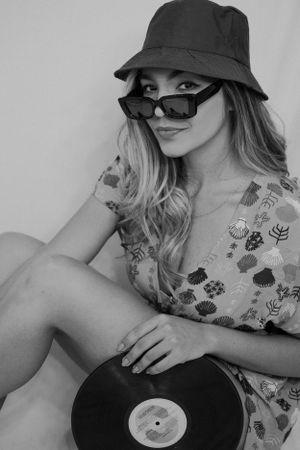 Black and white photo of someone in floral dress and bucket hat holding vinyl record.