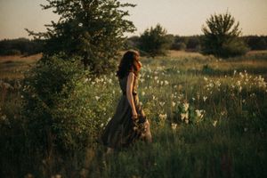 Figure in dark dress walking through wildflower meadow at golden hour.