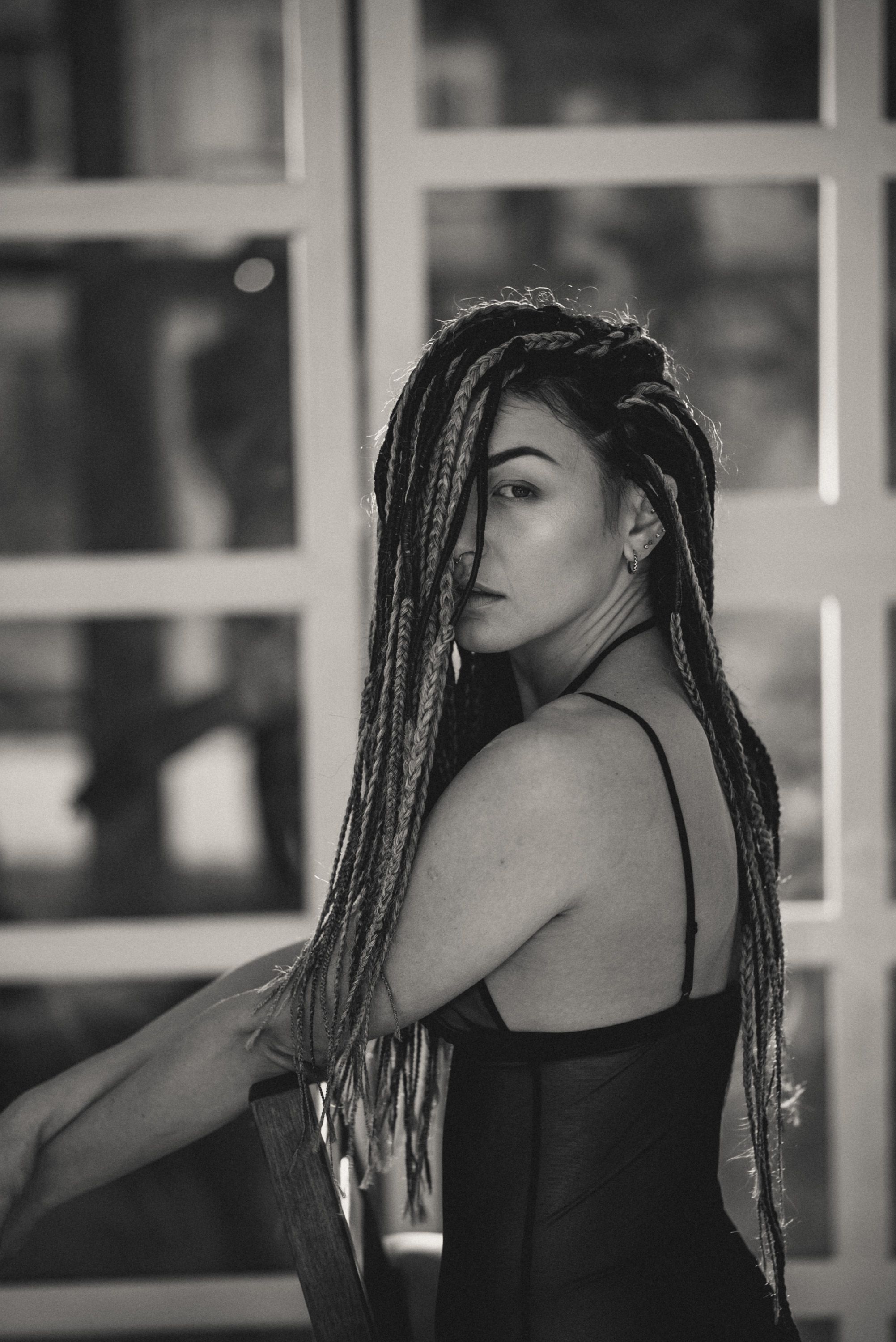 Black and white portrait showing long braided hair and dramatic side profile against a window background.