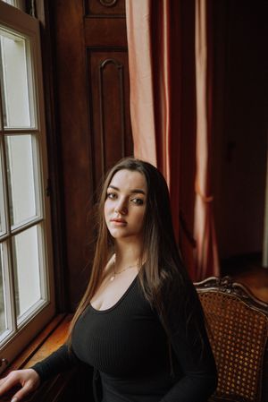 Moody indoor portraits by window with dark wood paneling and natural lighting.