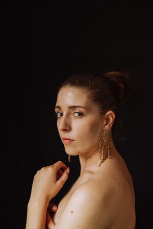 Studio portraits against dark background featuring ornate gold statement earrings and bare shoulders.
