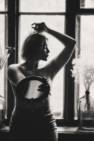 Silhouetted figure poses expressively by window with flowers in foreground.