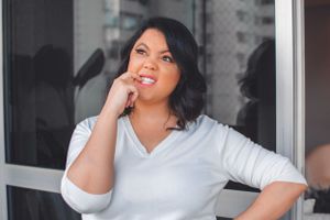 Person in white top smiling thoughtfully while posing against window.