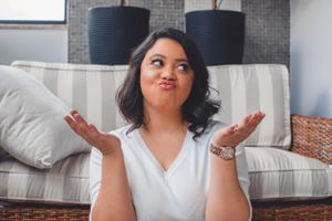 Person in white shirt gesturing with hands while sitting on gray couch.