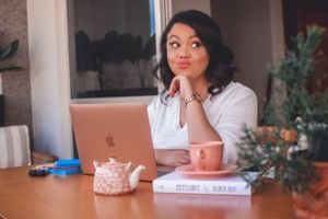 Person working at desk with MacBook, teapot, and pink teacup.