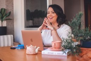 Person laughing while working at desk with laptop and pink tea set.
