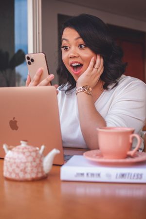Person showing excited expression while holding phone at desk with laptop.