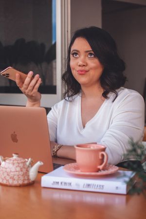 Person holding phone while working at desk with pink teacup and MacBook.