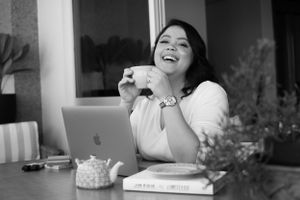 Black and white photo of person laughing while working at desk with laptop.