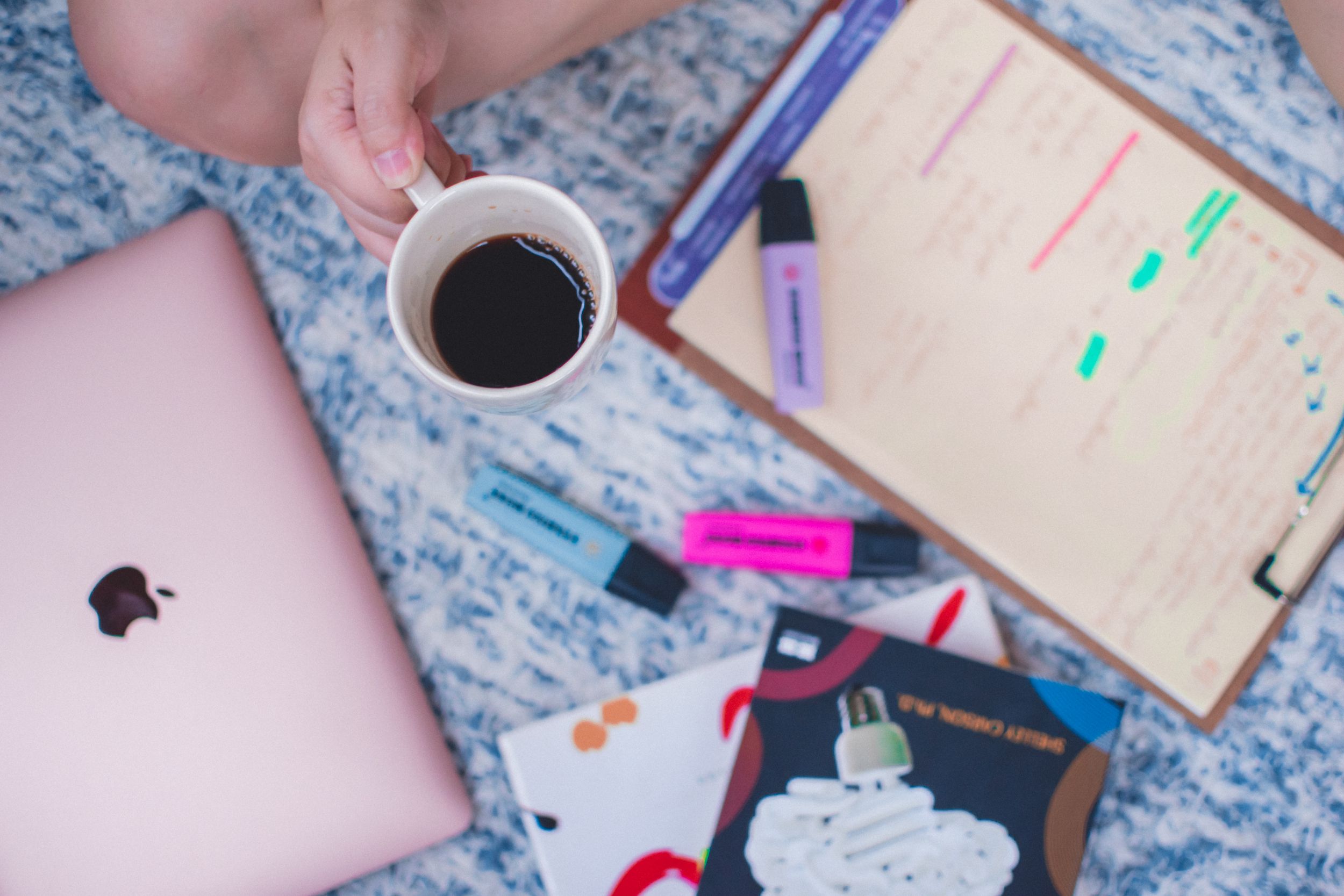 Flatlay of study essentials including notebooks, pens and coffee on a blue carpet.