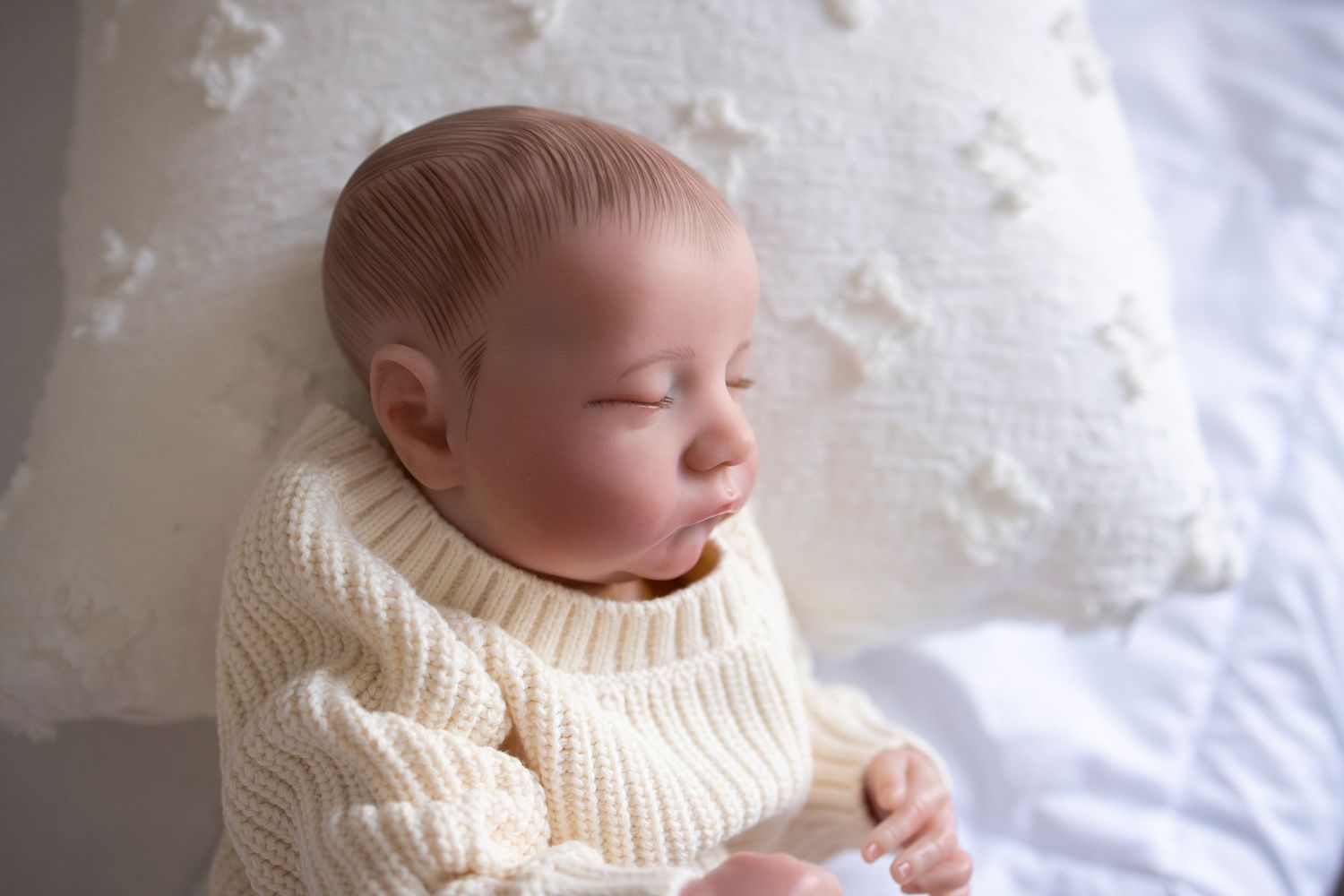 Baby doll laying on side with a cream sweater and white blanket.