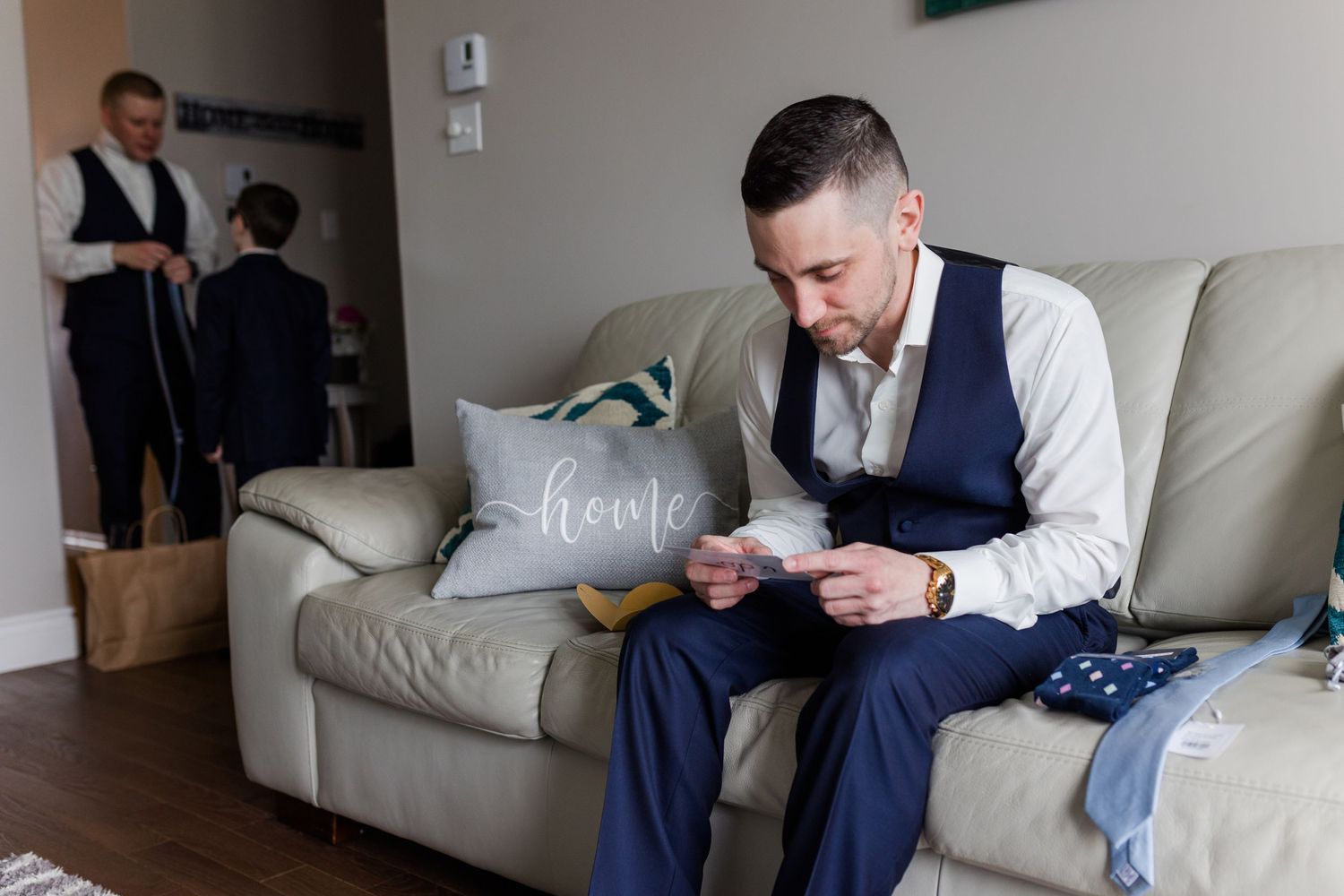 A person in formal attire sits on a beige couch reading papers during wedding preparations.