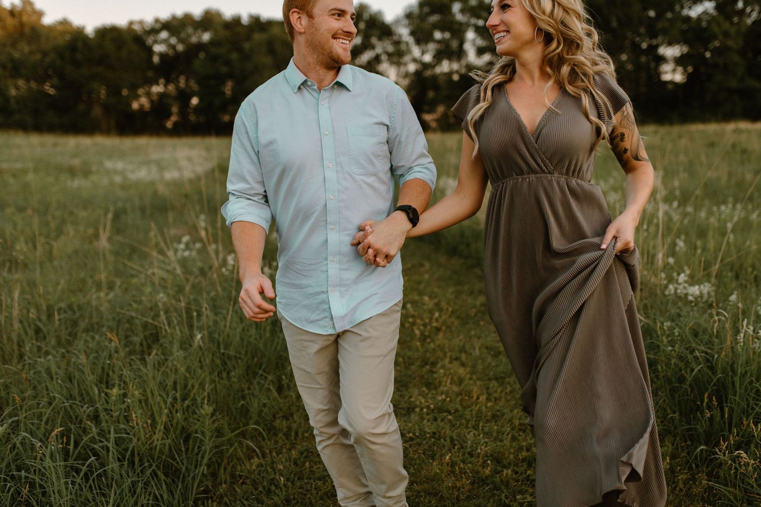 A couple shares laughter while walking through a grassy field in coordinated outfits.