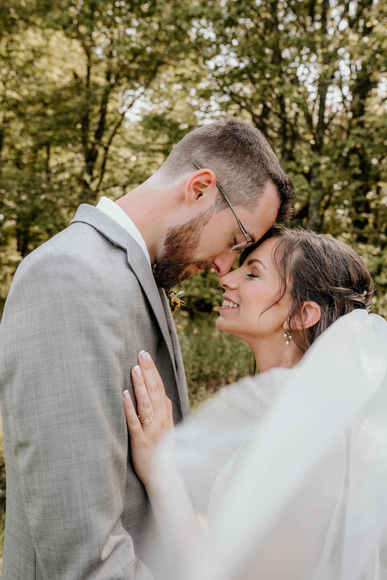 Bride and groom sharing an intimate forehead touch moment outdoors surrounded by lush green trees.