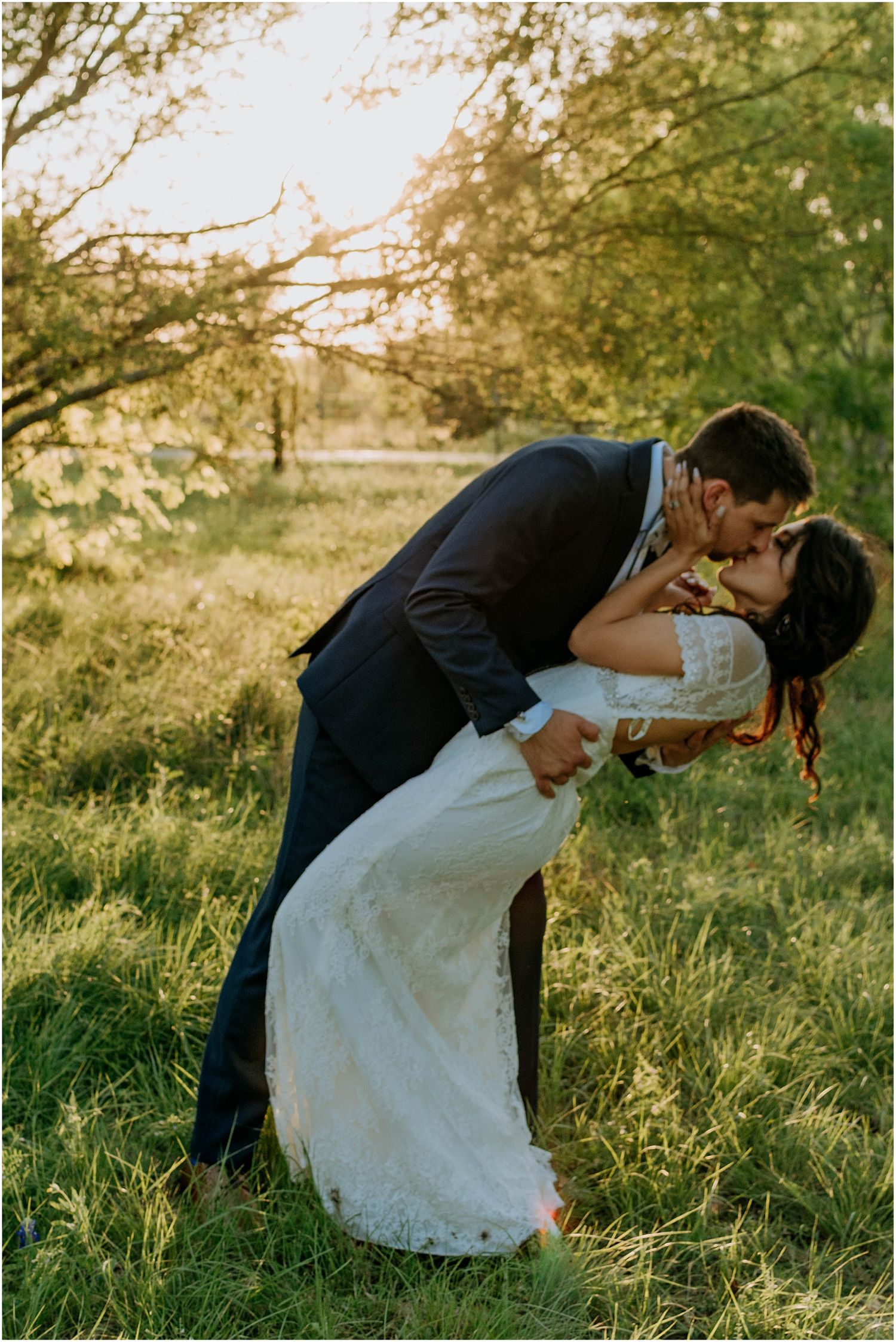 A romantic dip kiss between newlyweds in a sunlit field during golden hour.
