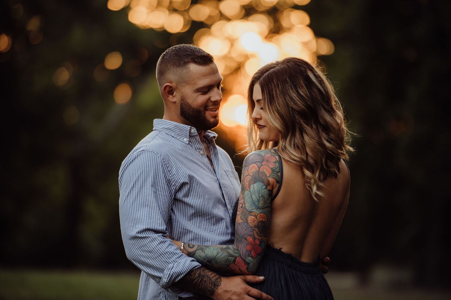 Romantic couple embracing during golden hour with bokeh lighting effects in background.