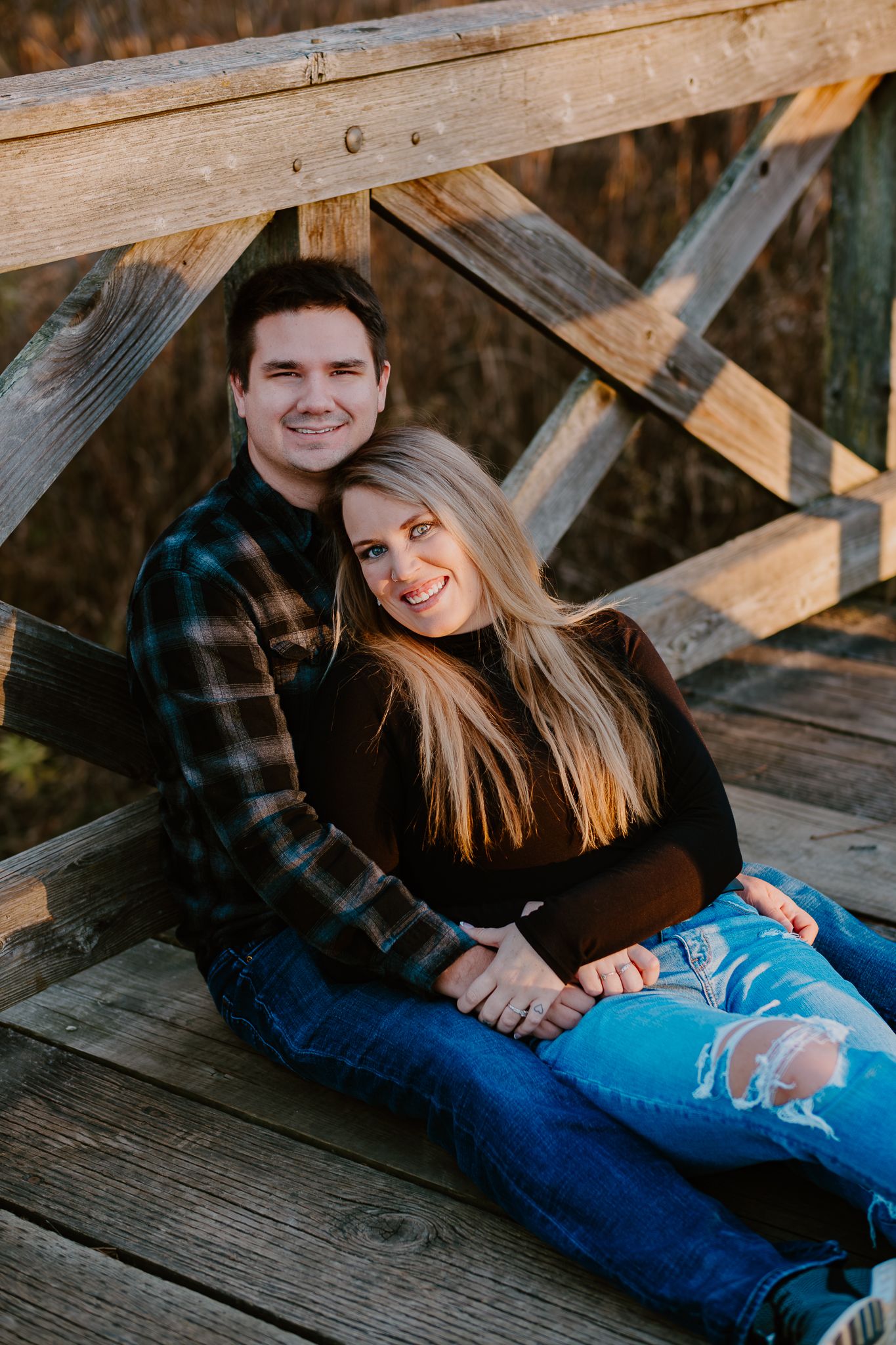 A couple relaxes together on a wooden deck during an autumn engagement photoshoot.