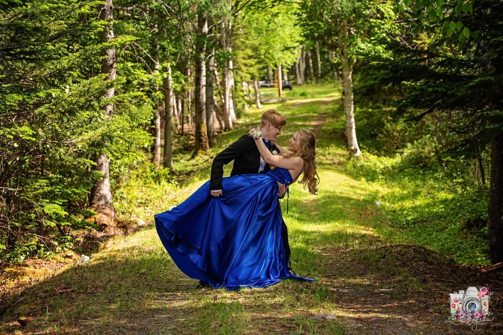 A person in a royal blue gown twirls on a forest path surrounded by trees.
