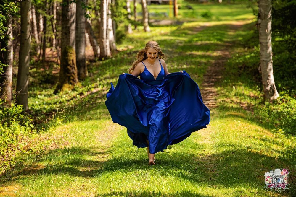 A person in a flowing blue gown leaps gracefully on a sunlit forest path.