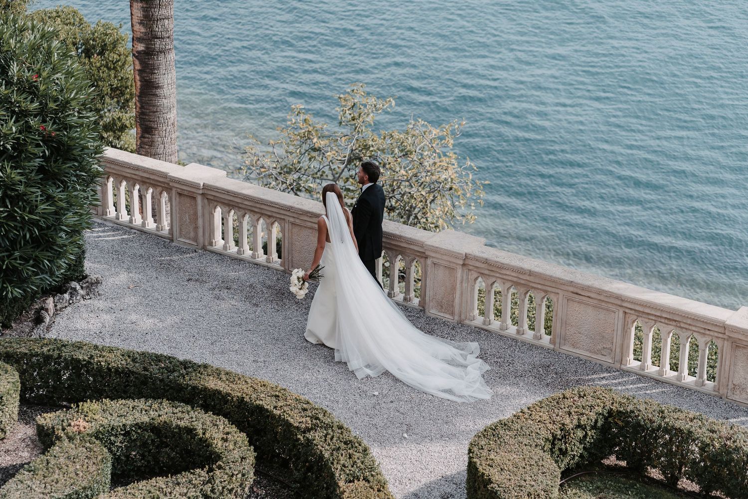 Bride and groom walking next to lake Garda in Italy hand in hand after getting married.