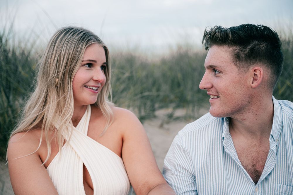 Romantic couple in white and striped outfits share intimate moments during outdoor photoshoot at sunset.