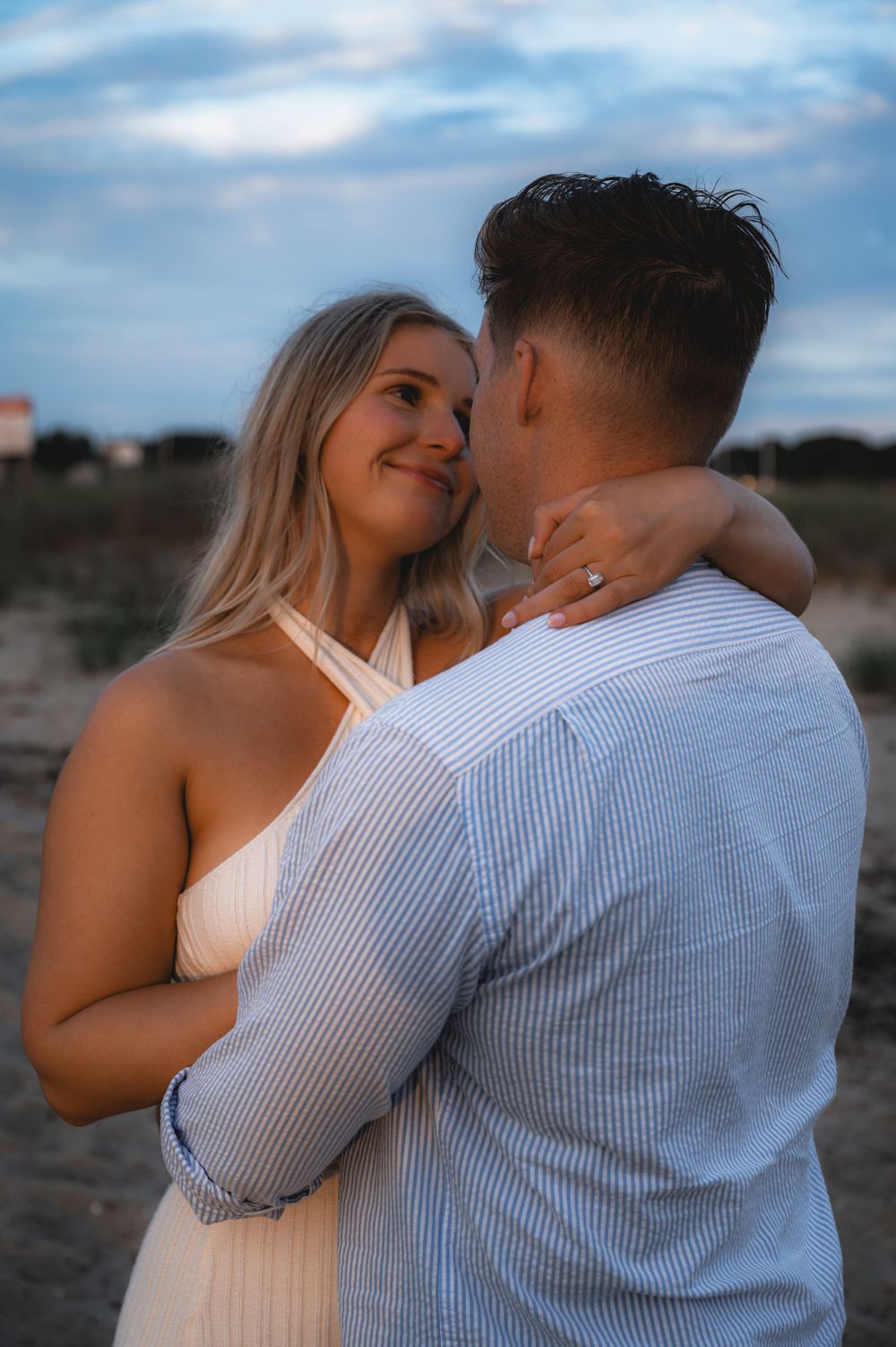 Couple shares intimate embrace during beachside photoshoot against blue sky.