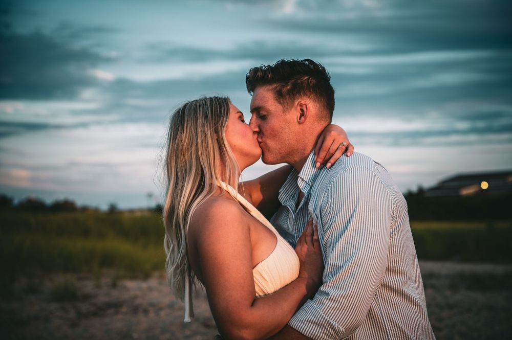 Couple shares romantic moments against dramatic teal sky during sunset photo session.