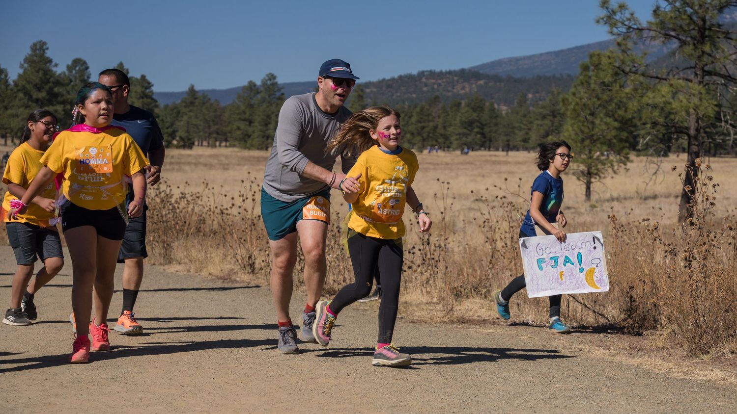 Runners participating in outdoor race along dirt path with mountains in background.
