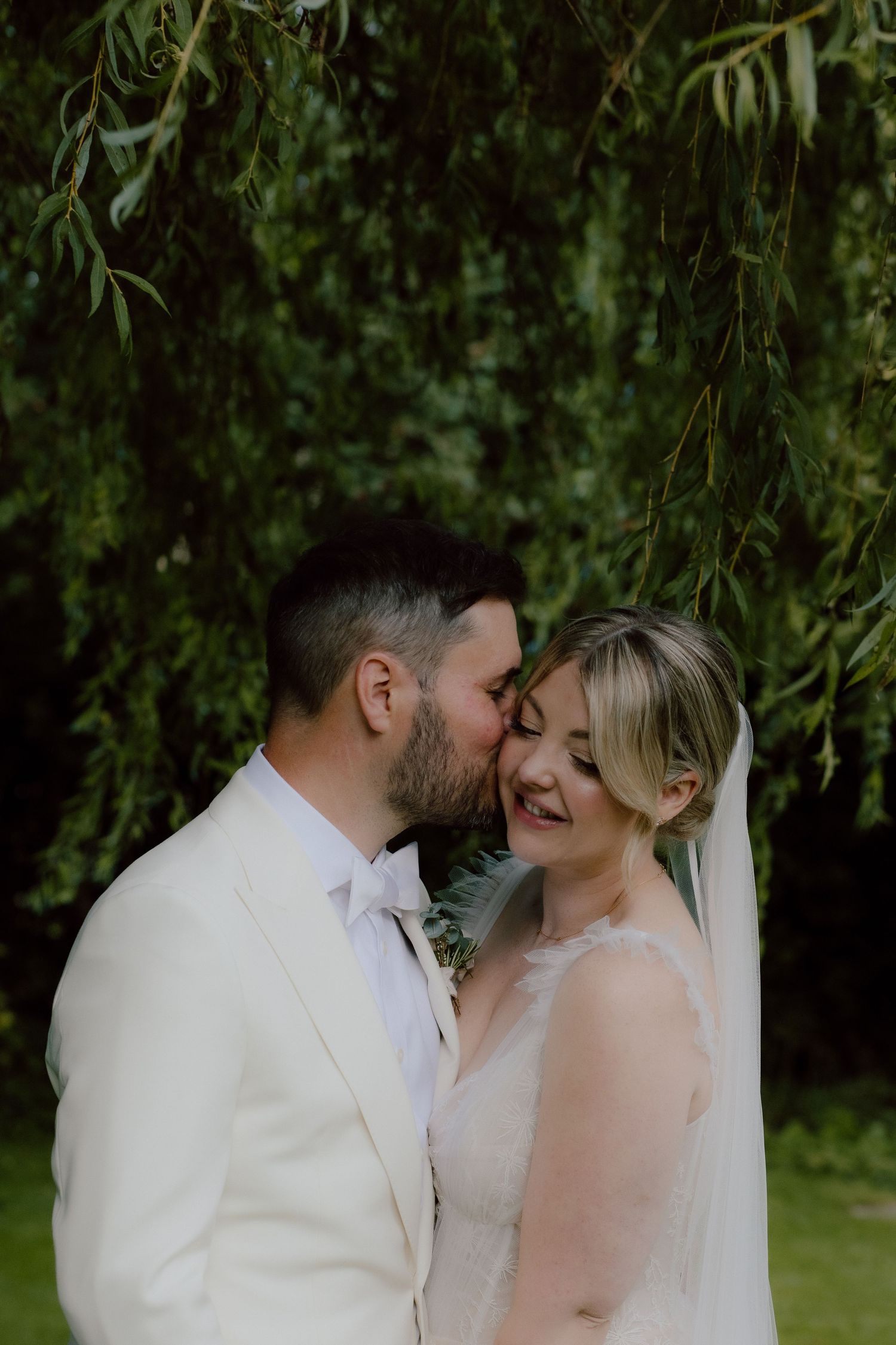 A romantic moment under weeping willow trees with the couple in elegant wedding attire.
