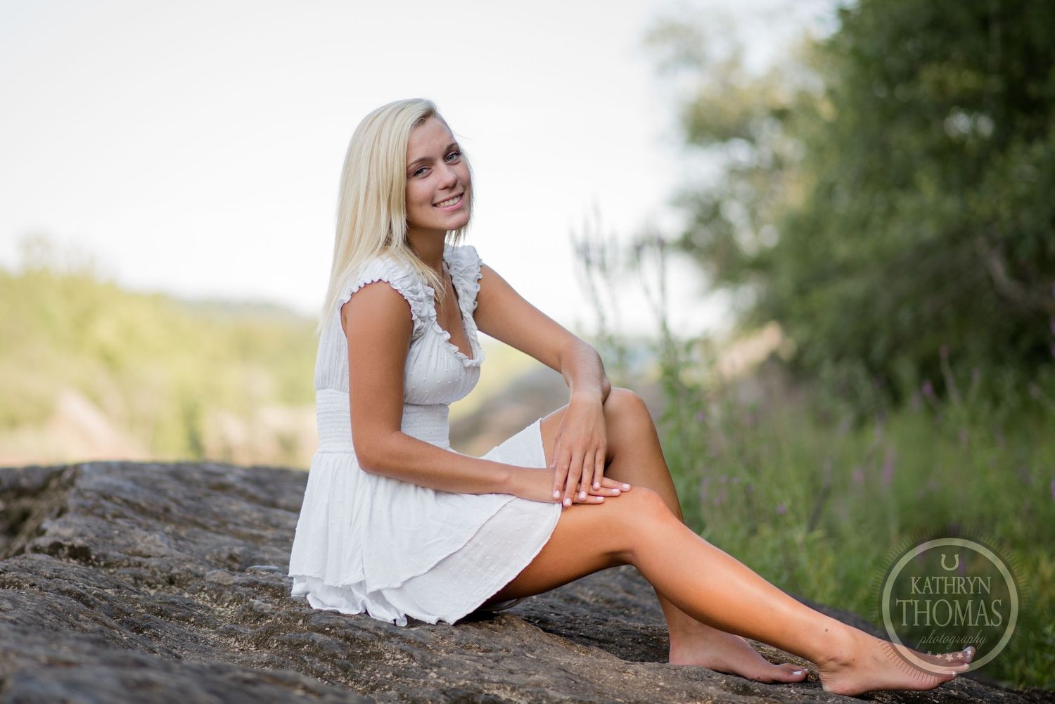 Outdoor portrait session features someone in white dress posed on large rock formation.