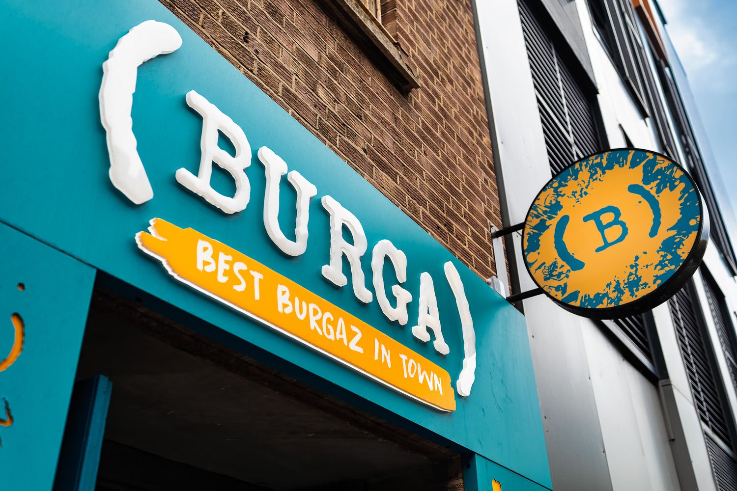 Burga restaurant teal signage with circular hanging sign against brick building exterior, commercial signage and branding photography