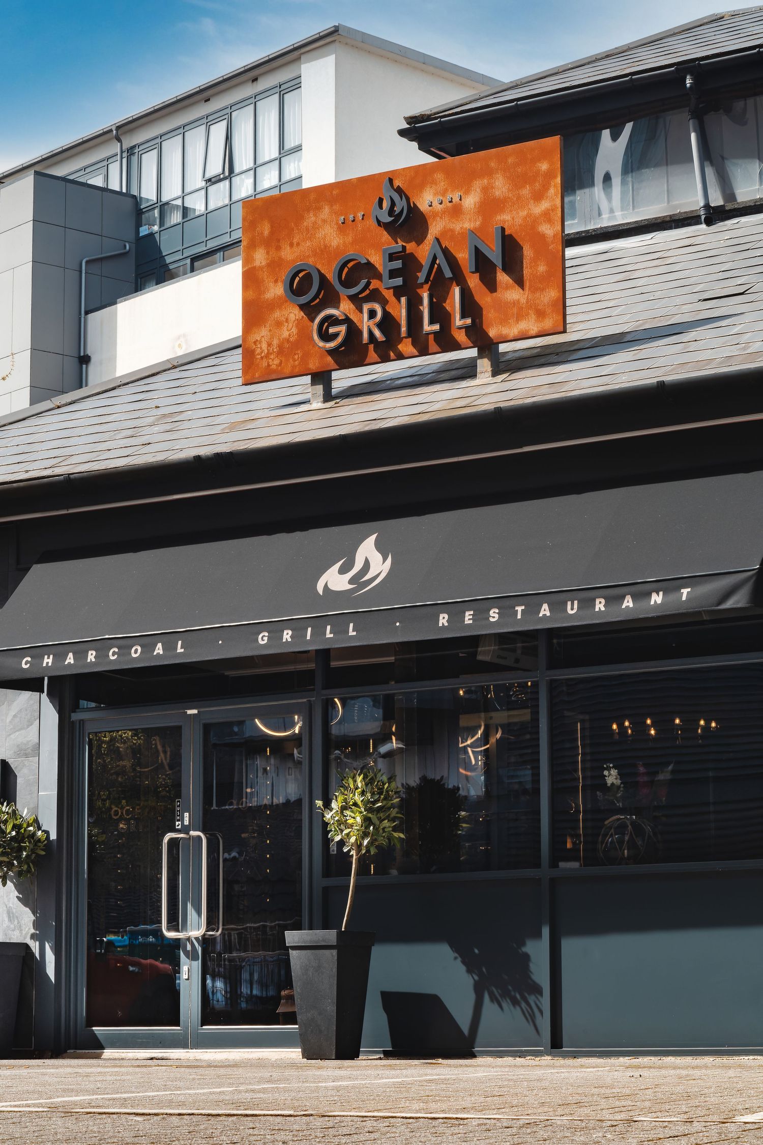 Ocean Grill restaurant exterior with orange signage, dark grey shopfront, glass windows and charcoal grill branding, commercial exterior pho